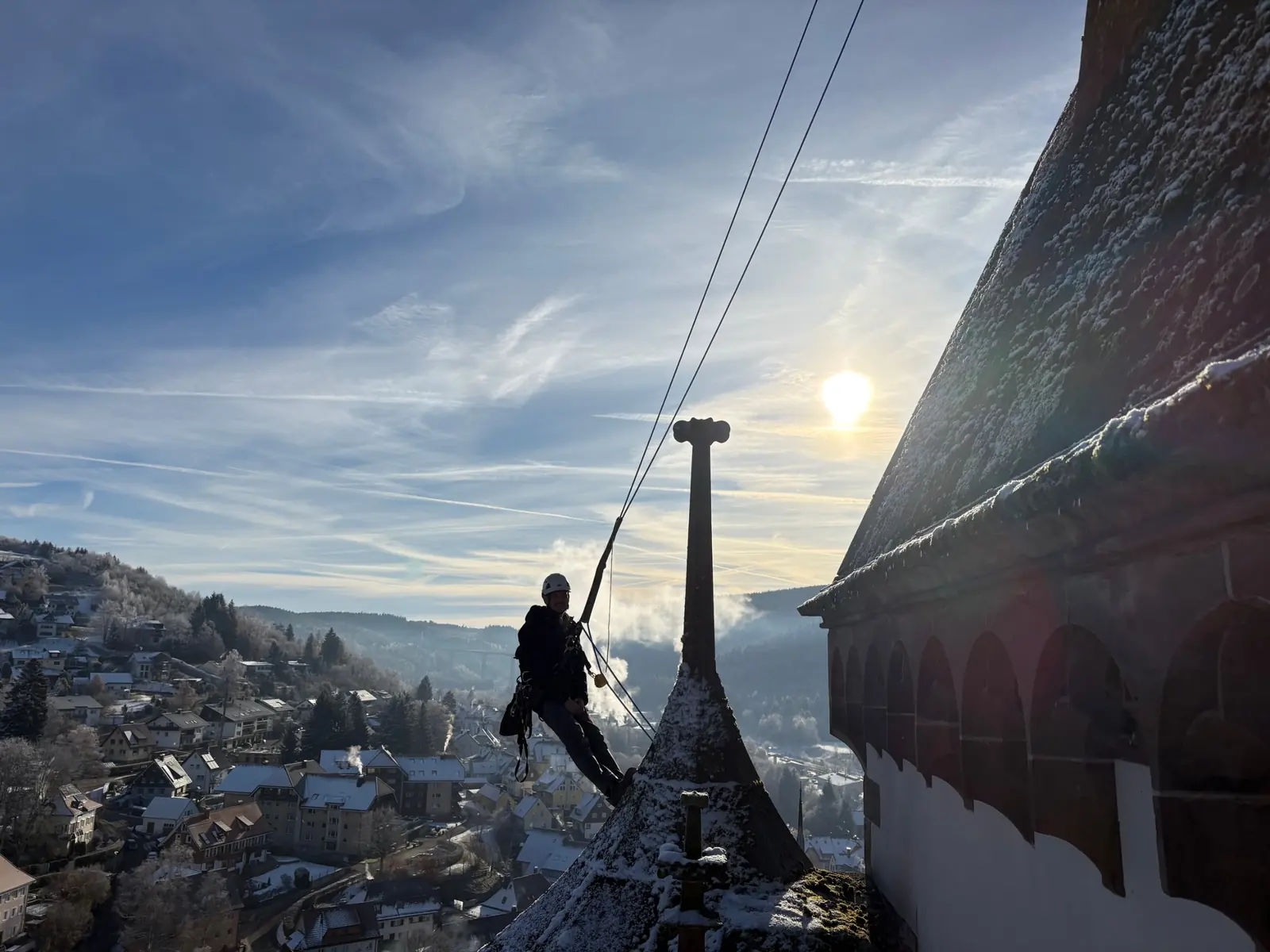 Industriekletterer an einer verschneiten Turmspitze mit Blick über die Dächer